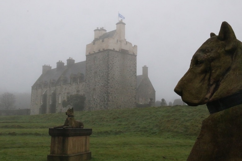 Two stone carved dogs in front of a castle building shrouded in mist