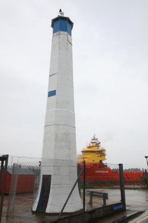 A small white tower at a harbour with a light at the top