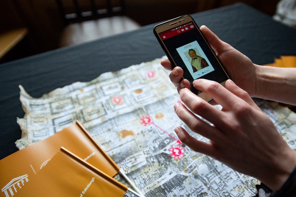 Close up of hands holding a smartphone which is scanning a hard copy map for more information