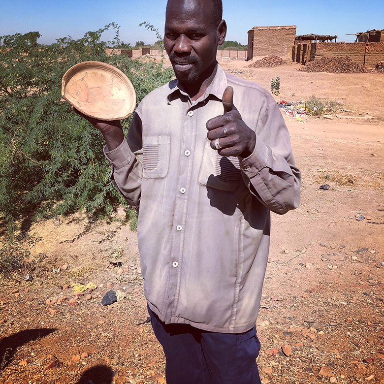 A man stands showing off a shallow bowl in one hand, giving the "thumbs up" sign with his other hand.