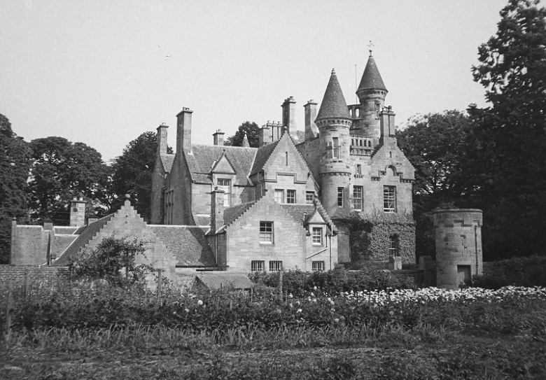 Black and white image of a grand, turreted country house set in woodland