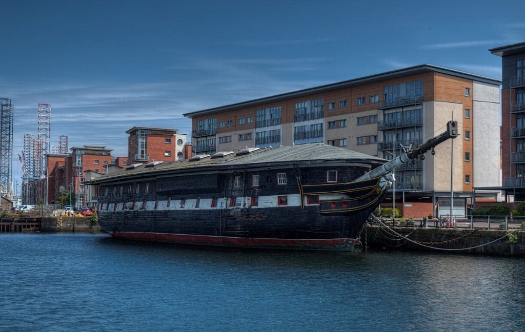 View of the HMS Unicorn at the riverside in Dundee. The ship is curved and wooden, with a roof covering the top deck