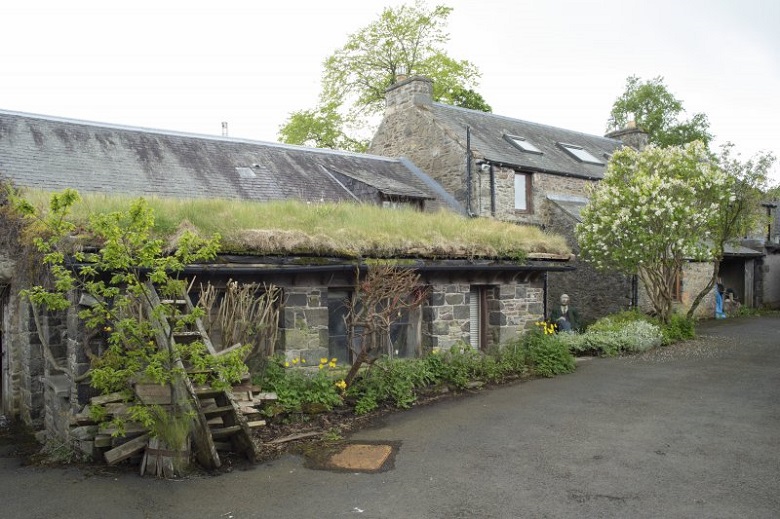 The exterior of The Steading, appearing as an unassuming stone farmhouse surrounded by green plants 