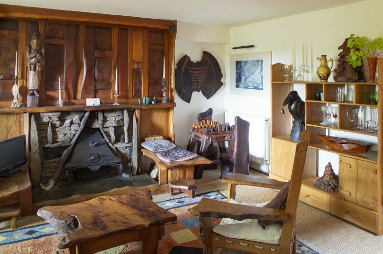 A living room inside The Steading full of wooden furniture and furnishing. An intricately carved figure features above the fireplace. 