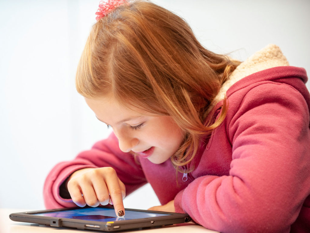 A girl in a pink jacket smiling as she uses a tablet