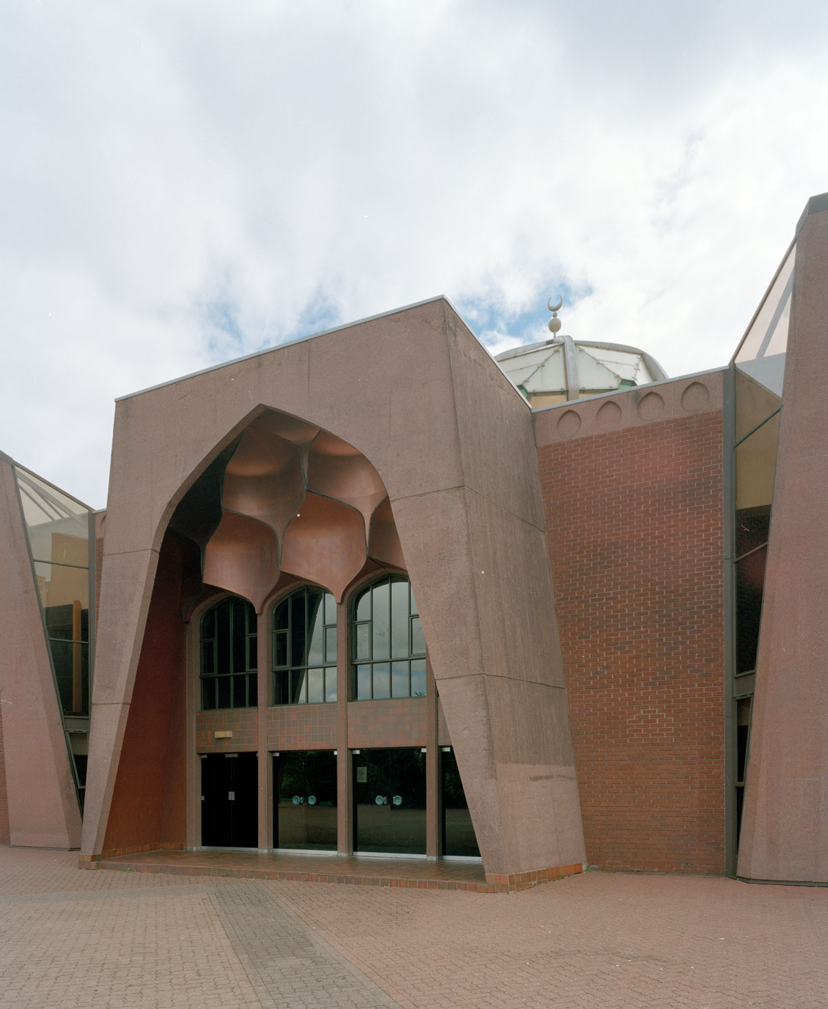 red brick and concrete arch over the entrance to a mosque with glass windows and doors