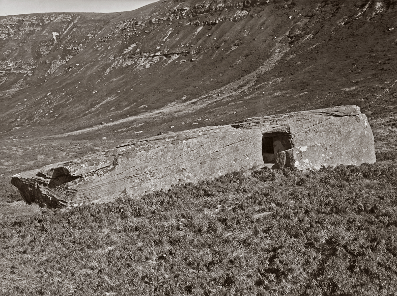 A black and white photo of a large hollowed-out stone in a remote glen