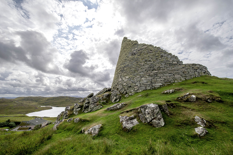 A close up shot of a dry stone broch on a grassy and rocky mound