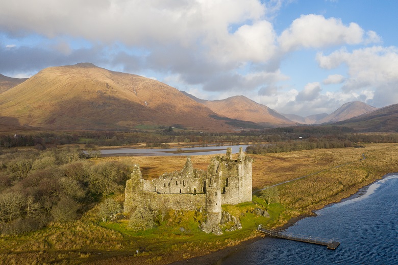 A pier jutting out into Loch Awe in front of the ruins of Kilchurn Castle
