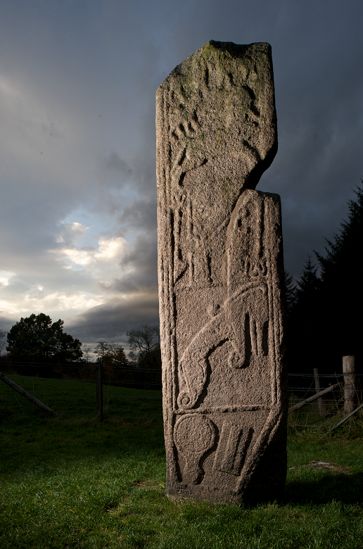 A Pictish stone photographed at dusk featuring stone carvings of animals and beasts