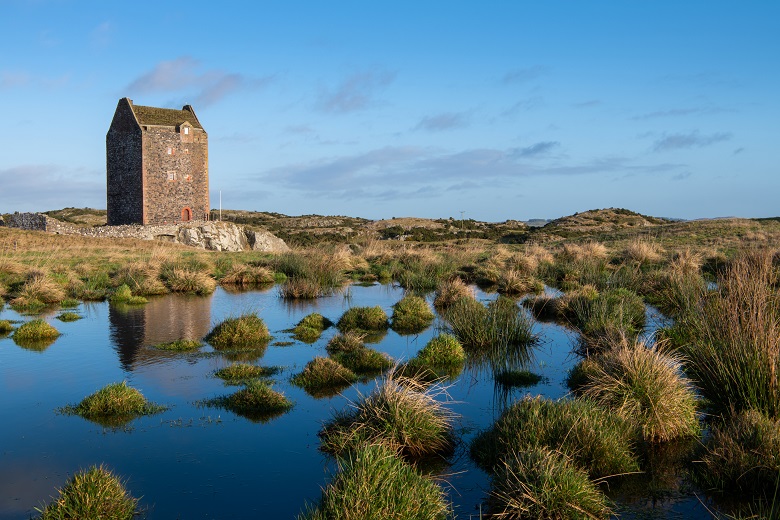 A small pond in front of a fortified tower house in winter sunshine.