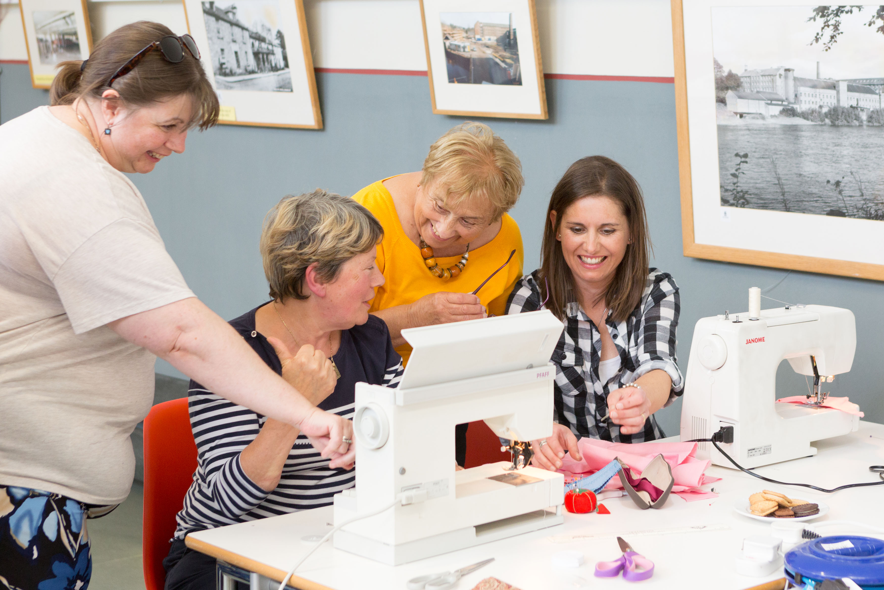four women gathered around a sewing machine laughing and chatting