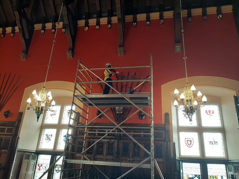 A scaffold erected in the great hall of a castle to allow staff to clean weapons hanging high on the walls