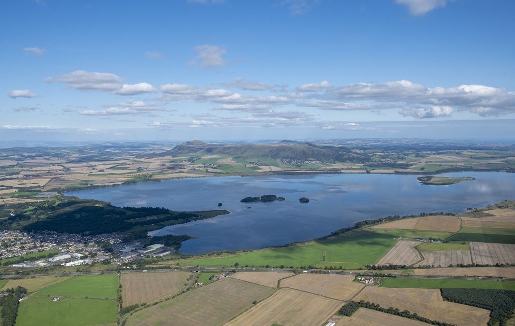 An aerial view of a loch and the surrounding landscape including farmland and a town