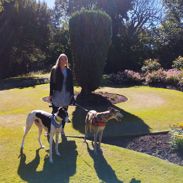 a woman with two greyhounds on leads in a formal garden.