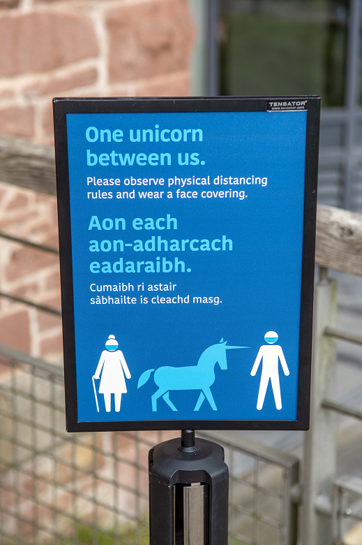 A sign in English and gaelic encouraging social distancing by requesting visitors keep "one unicorn" apart