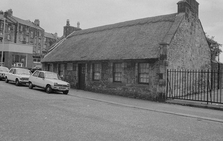 Black and white archive photo of a small thatched cottage on an urban street