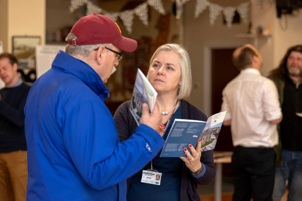 A woman speaks to a man wearing a red cap in a community hall