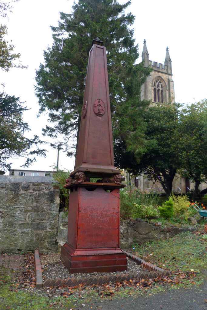A large red cast-iron monument stands in front of a church