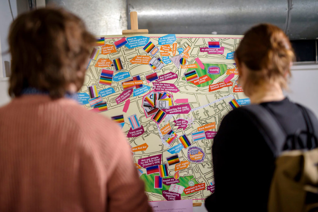 Two people look at a map annotated with events and covered in variations of the Gay Pride Rainbow Flag