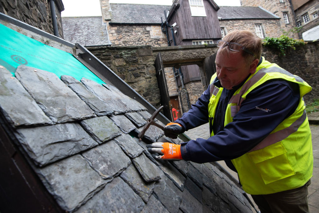 A man in a high visibility jacket and wearing gloves repairs the tiles of a roof