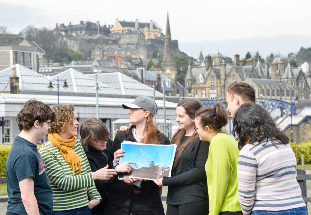 A group of young people in front of Stirling Castle looking at a photograph of an industrial crane