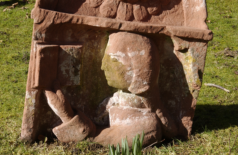 A historic gravestone with a figure reading a book carved on it 