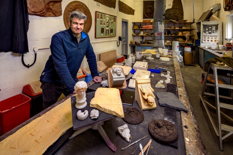 A person standing at a table with historic pieces of stone on it