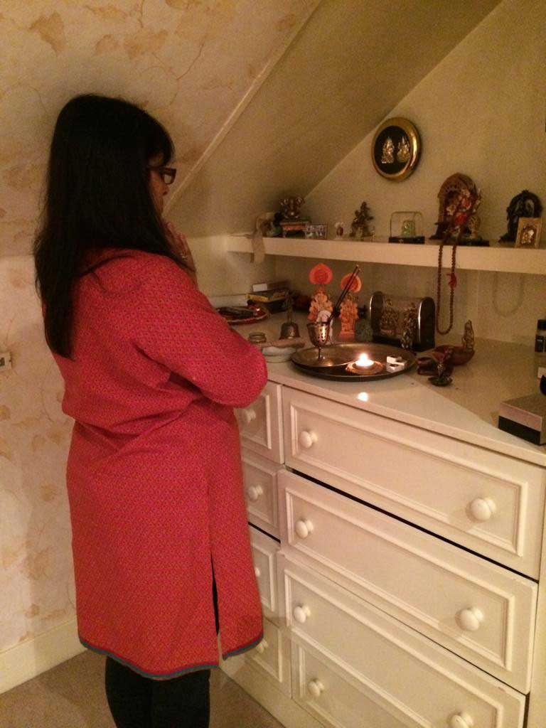 A woman prays by a small shrine on a chest of drawers in a home