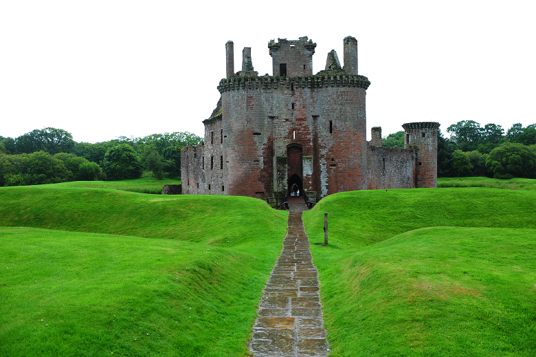 A path approaching the gatehouse of a ruined castle, accessed via a bridge