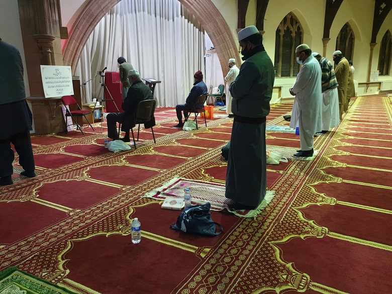 Men in traditional Muslim dress attend prayer in a socially distanced manner