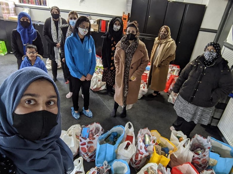 A group of Muslim women wearing covid face masks stand around bags of groceries at a food bank