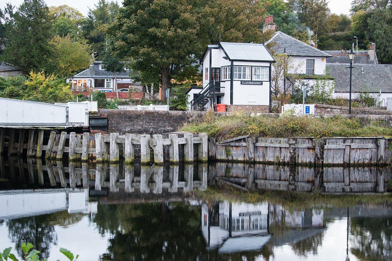 A small black and white railway station building located beside a canal