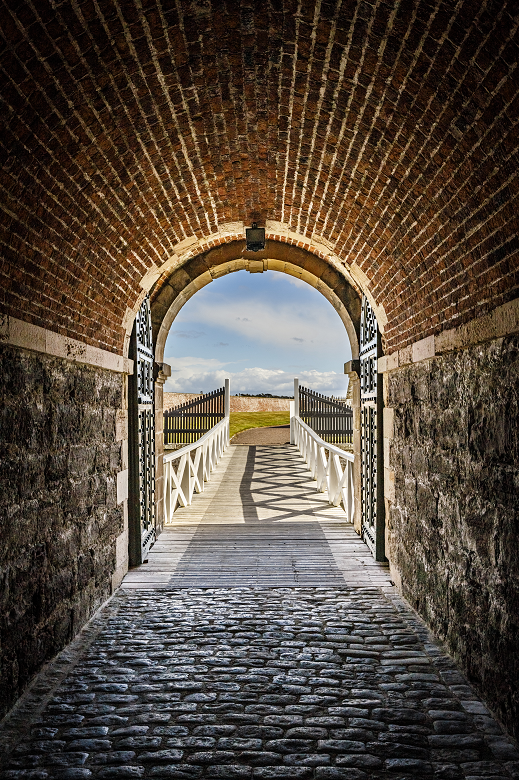 The entrance to a military fort through a stone archway and over a bridge