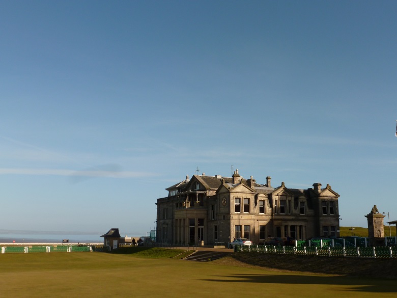 A large golf clubhouse under a cloudless blue sky, with an immaculate golf green in the foreground
