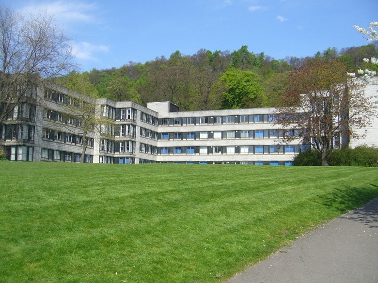 Grass in front of a 1960s university building, with a tree-covered hill in the background