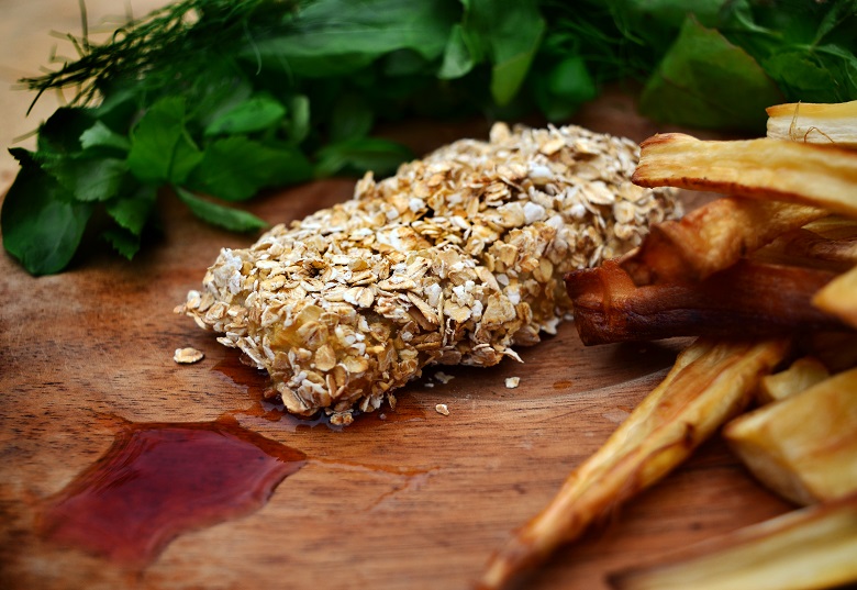 A piece of fish coated in oats served alongside chips and a ketchup made from vegetables 