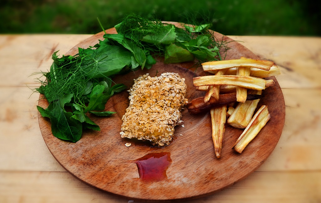 A medieval take on fish and chips presented on a round wooden board with green leaves and red sauce