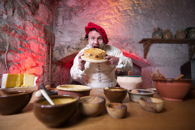 A living history performer tucks into a large meat pie in a recreation of a medieval castle kitchen