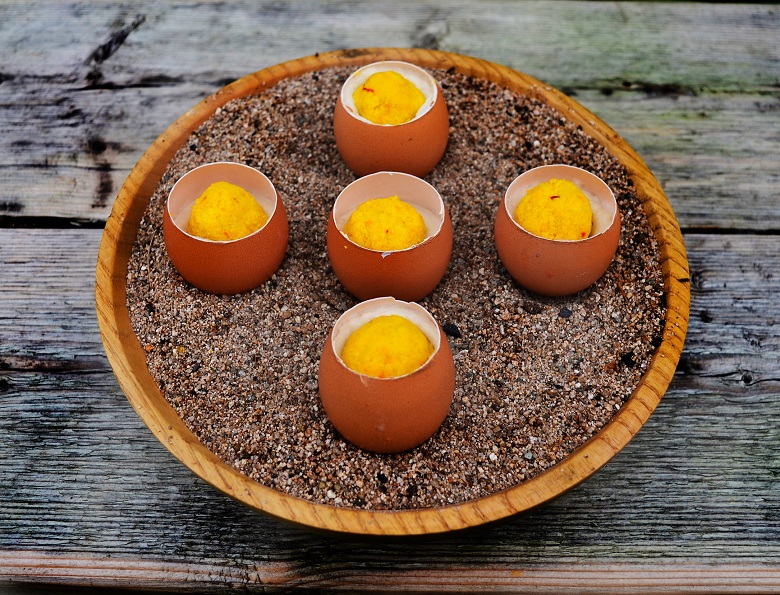 5 eggshells filled with sweet ingredients arranged in a cross shape on a round wooden plate