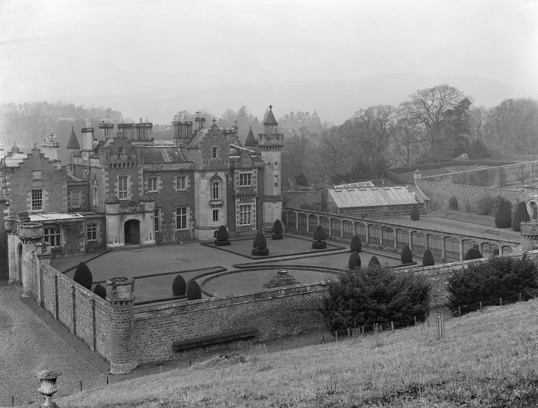 A black and white photo of Walter Scott's farmhouse-turned-mansion at Abbotsford. The ornate house can be seen backing onto a carefully maintained walled garden 