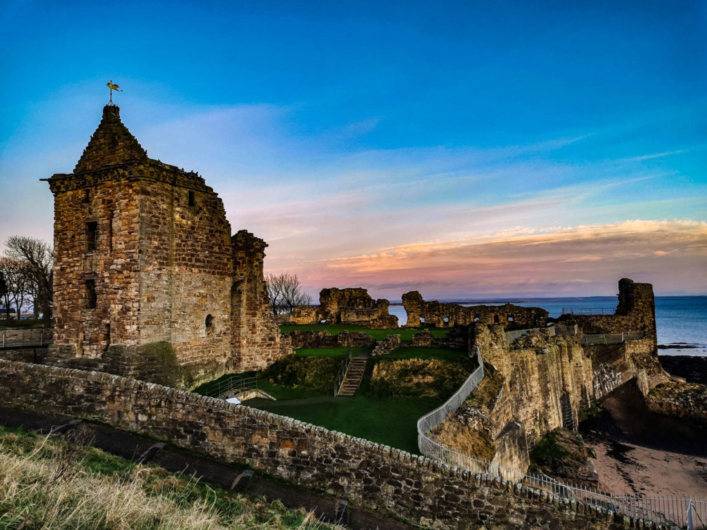 An atmospheric scene of the ruins of St Andrews Castle beside the sea as the sun sets