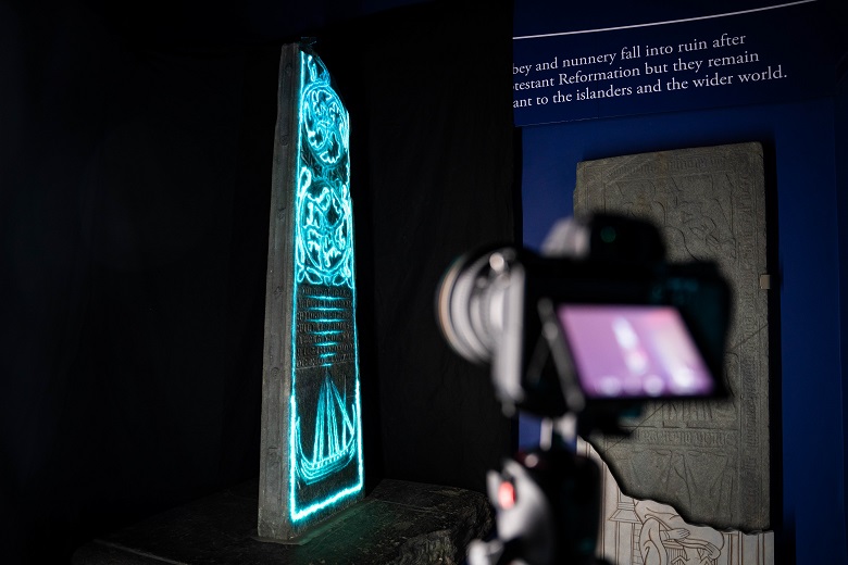 The view from behind a camera capturing images of a projection onto a carved standing stone