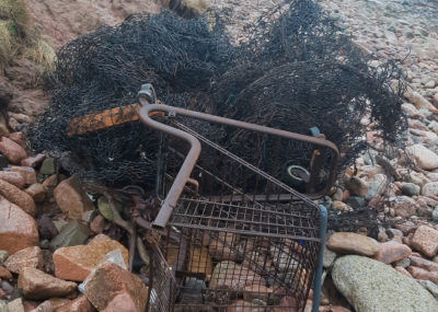 An old shopping trolley rusts on a beach