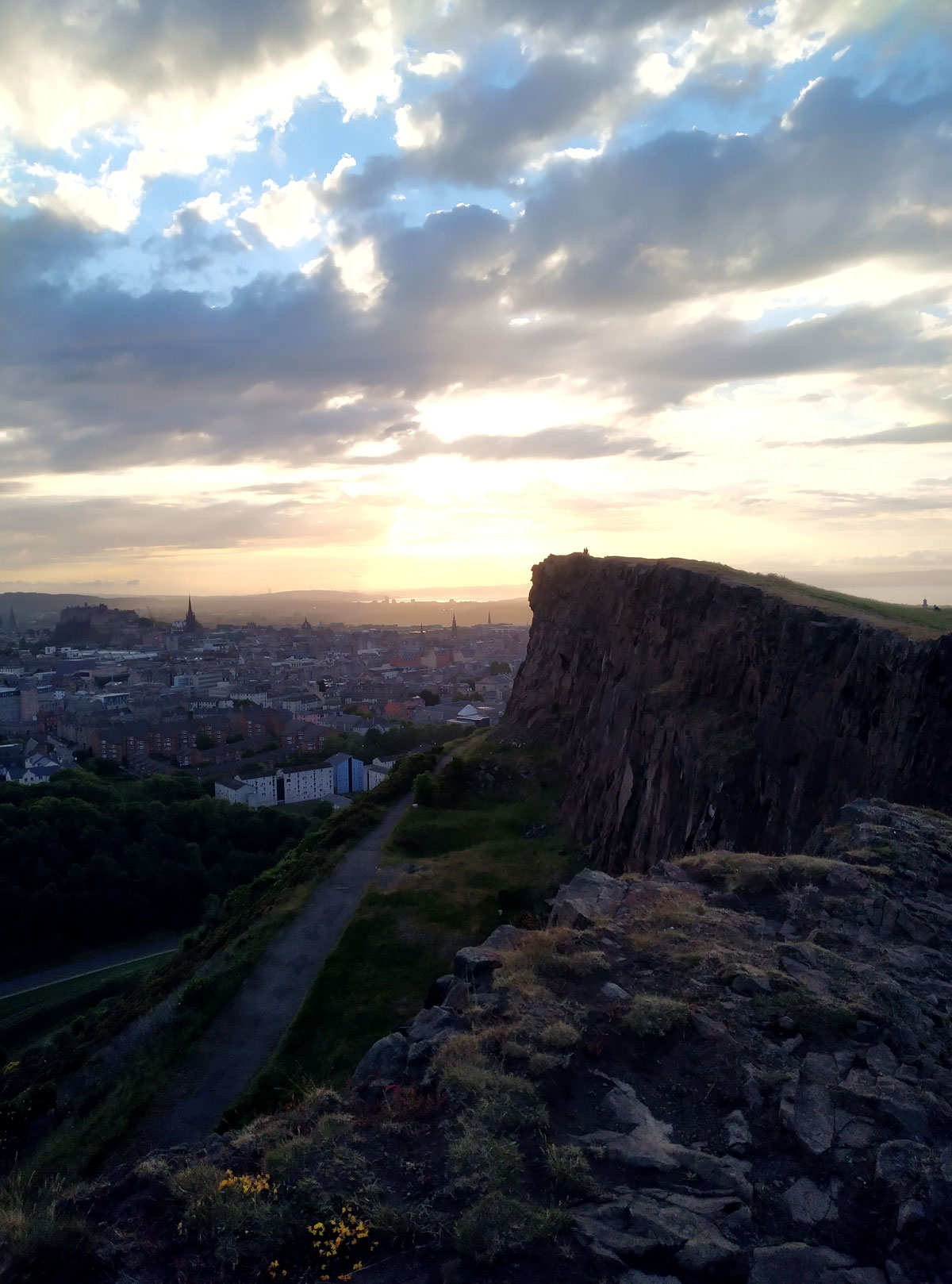 A sunrise with the city of Edinburgh silhoutted and the crags in the forefront