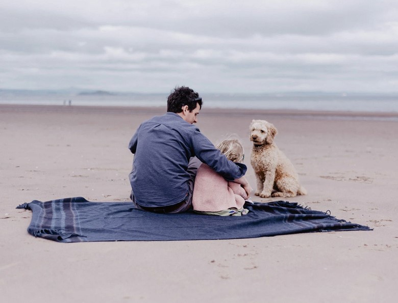 family sitting on a blanket at the beach with their dog