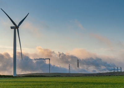 A landscape that includes a wind turbine, electricity pylons and a smoking chimney