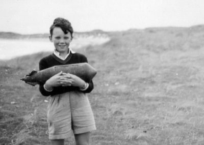 A black and white photograph of a young boy holding items found on a beach