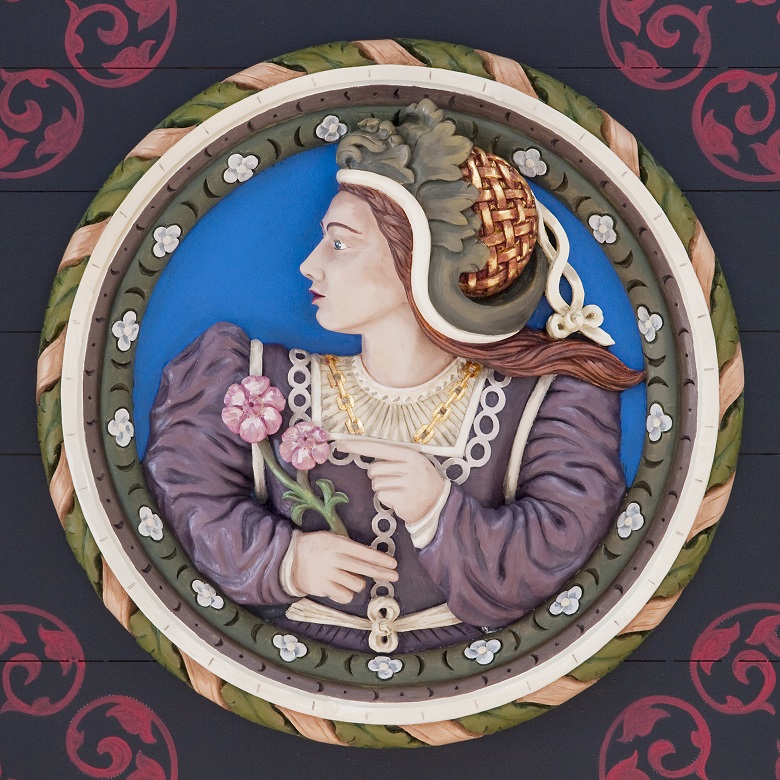 A colourful wooden carving depicting a women wearing an elaborate purple dress and green headwear. She is holding two pink roses.