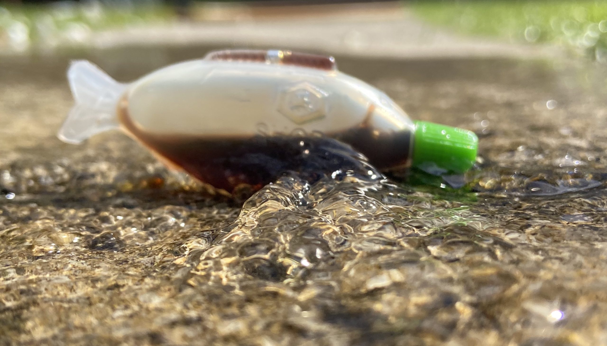 A fish shaped plastic bottle with soy sauce sits in a puddle.